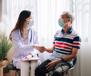 Asian doctor visit and examines a senior man at home ,shaking hands after finished health check up ,hospital services ,and wearing a mask to protect covid-19.